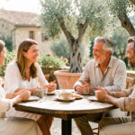 Élargir son cercle social en PACA : activités et sorties locales Groupe de deux femmes et deux hommes adultes échangeant chaleureusement autour d’une table sur une terrasse ensoleillée de Provence.